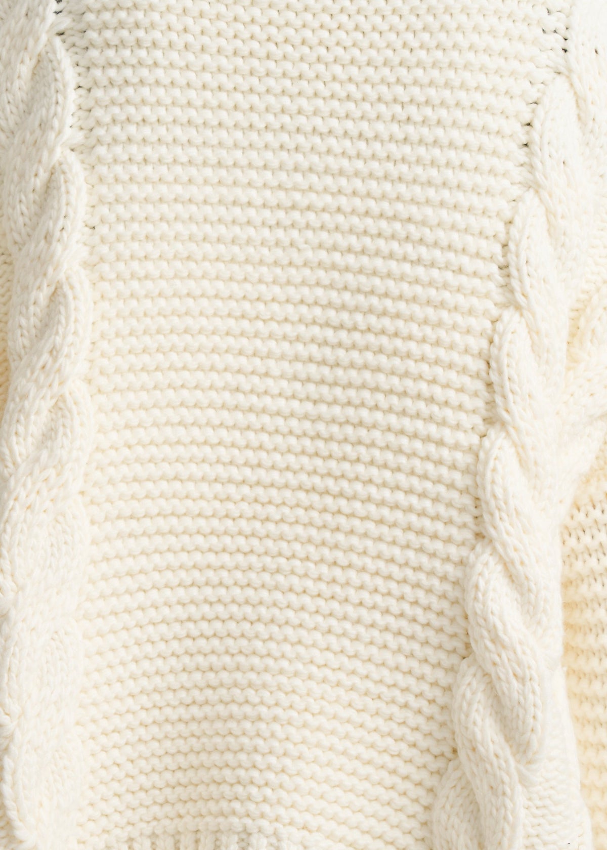 Close-up of a cream-colored cable-knit sweater showing the detailed knit texture and twisted cable patterns.