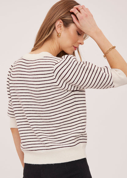 A woman wearing a cream knit sweater with thin black horizontal stripes, shown from the back and side against a plain light background.