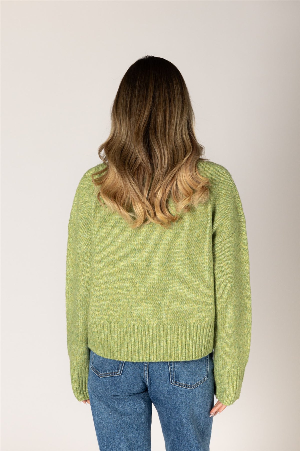Person wearing a green sweater and blue jeans against a plain background
